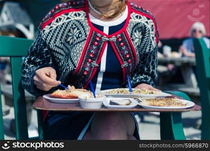 A young woman is eating cokcles and smoked fish outside on a sunny day
