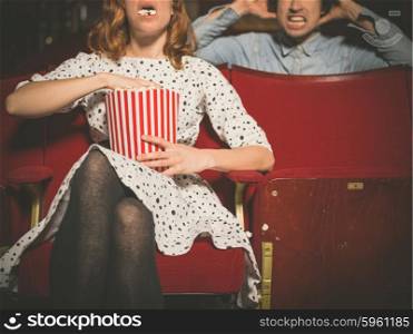 A young woman is eating popcorn loudly in a movie theater and is annoying the man sitting behind her