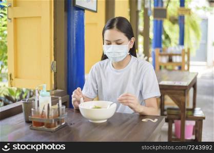 A young woman is eating Thai Street food , wearing face mask, New normal eating concept