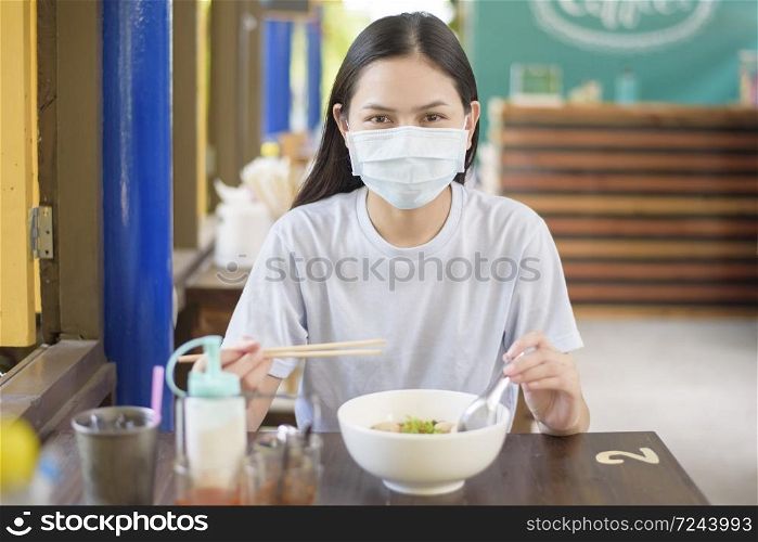 A young woman is eating Thai Street food , wearing face mask, New normal eating concept