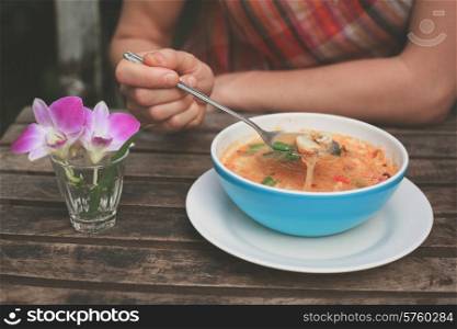 A young woman is eating tom yum soup at a table outside