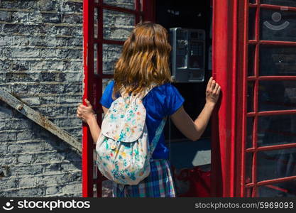 A young woman is entering a traditional red english phone booth on a sunny day