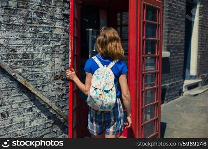A young woman is entering a traditional red english phone booth on a sunny day