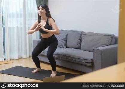 A young woman is exercising and watching online training fitness class on the laptop in living room at home, sport, fitness and technology concept.. Young woman is exercising and watching online training fitness class on the laptop in living room at home, sport, fitness and technology concept.