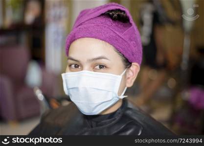 a young woman is getting a haircut in a hair salon , wearing face mask for protection covid-19 , salon safety concept