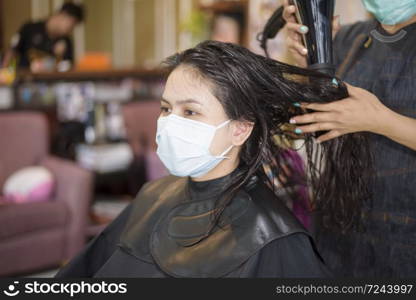 a young woman is getting a haircut in a hair salon , wearing face mask for protection covid-19 , salon safety concept