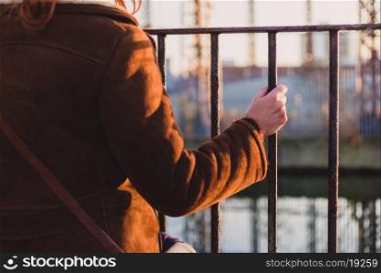 A young woman is grabbing a fence by a canal in the winter