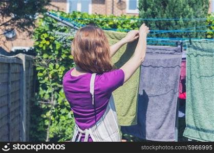 A young woman is hanging her laundry on a clothes line in the garden on a sunny day