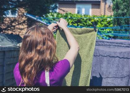 A young woman is hanging her laundry on a clothes line in the garden on a sunny day