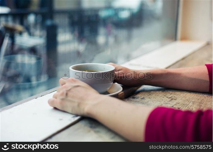 A young woman is having a coffee by the window in a cafe