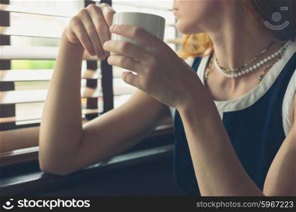 A young woman is having a cup of coffee by the window in a diner