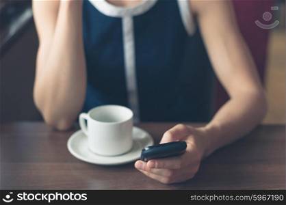 A young woman is having a cup of coffee in a diner and is using her smartphone