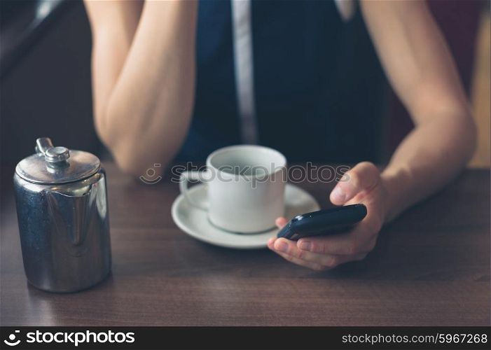 A young woman is having a cup of coffee in a diner and is using her smartphone