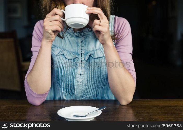 A young woman is having tea or coffee at a table in a dining room