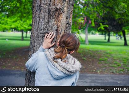 A young woman is hiding behind a tree in the park