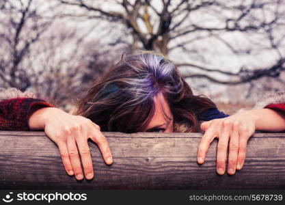 A young woman is hiding behind a wooden beam in the park
