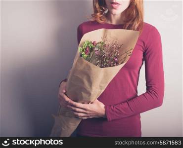 A young woman is holding a bouquet of flowers indoors against a purple wall