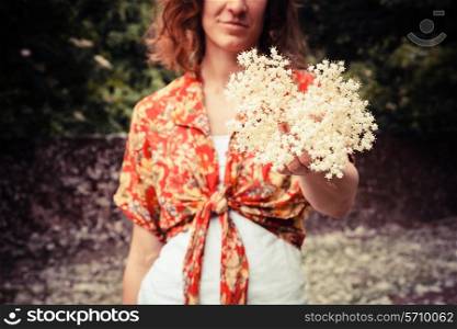 A young woman is holding a bunch of elderflowers she has been picking