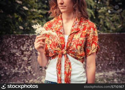 A young woman is holding a bunch of elderflowers she has been picking