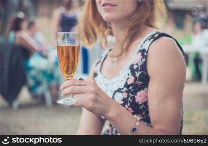 A young woman is holding a flute with a beverage outside at a party