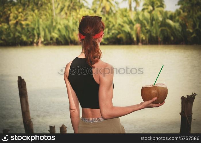A young woman is holding and drinking from a coconut by a river in the tropics