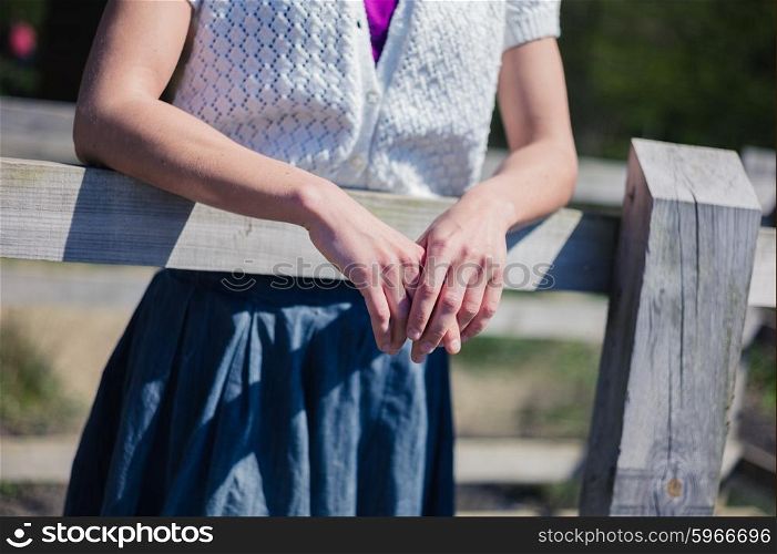 A young woman is leaqning on a fence outside and is resting