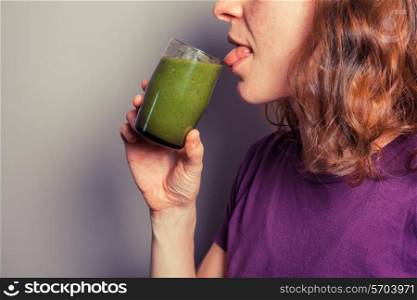 A young woman is licking a glass filled with green smoothie