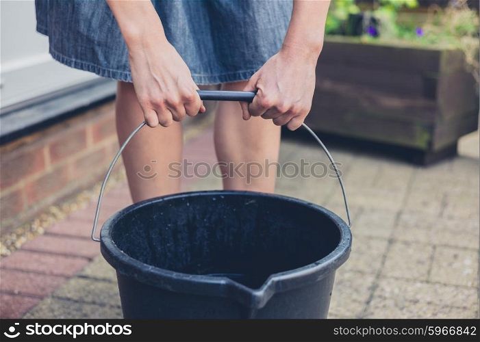 A young woman is lifting a big bucket outside in a garden