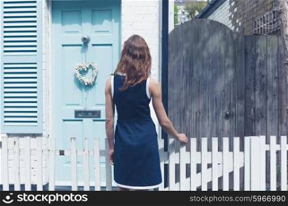 A young woman is looking at a little house with a blue door