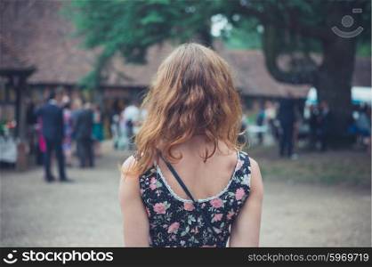 A young woman is looking at a party taking place at an old house in the countryside