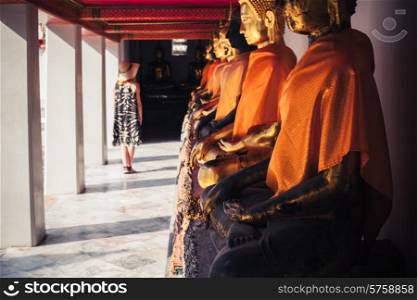 A young woman is looking at a row of buddha statues in a temple