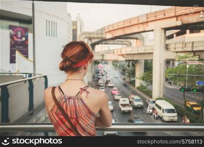 A young woman is looking at the traffic from an overpass in Bangkok
