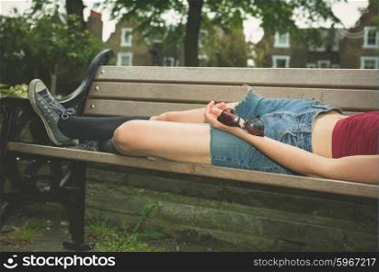 A young woman is lying down and relaxing on a park bench on a sunny summer day
