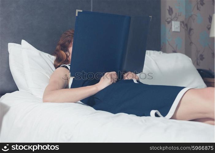 A young woman is lying on a bed in a hotel room and is reading the hotel information