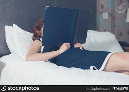 A young woman is lying on a bed in a hotel room and is reading the hotel information