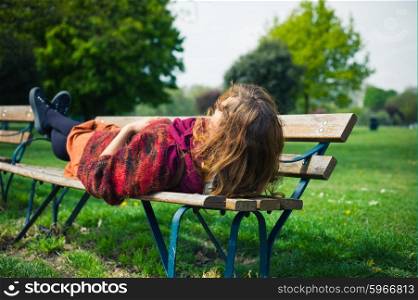 A young woman is lying on a bench and is relaxing in the park on a sunny spring day