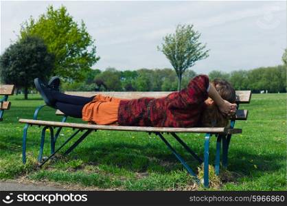 A young woman is lying on a bench and is relaxing in the park on a sunny spring day