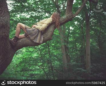 A young woman is lying on a branch of a tree in the forest