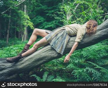 A young woman is lying on a fallen tree in the forest surrounded by ferns