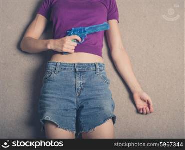 A young woman is lying on the carpet at home with a blue water pistol in her hand