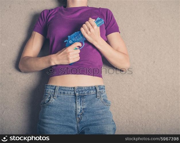 A young woman is lying on the carpet at home with a blue water pistol in her hand