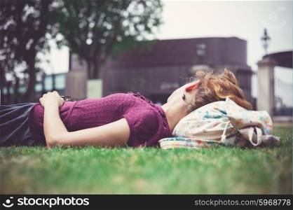 A young woman is lying on the grass in a park and is relaxing