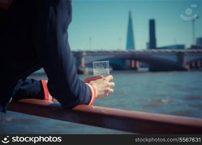 A young woman is on a boat on the Thames in London and holding a glass of water