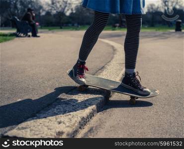 A young woman is performing a skateboard trick on the curb in a park