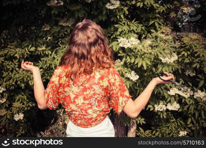 A young woman is picking elderflowers and is looking confused