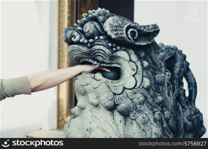A young woman is playing with the balls in the mouth of a Chinese lion statue