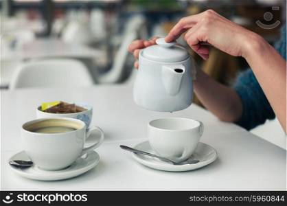 A young woman is pouring a cup of tea in a cafe