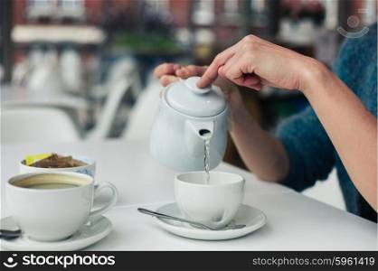 A young woman is pouring a cup of tea in a cafe