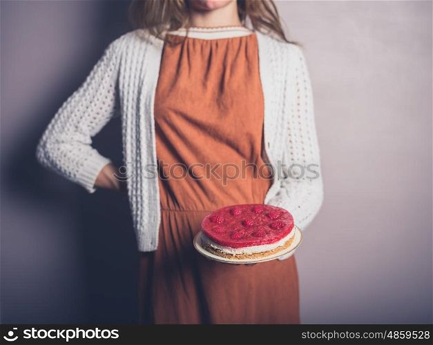 A young woman is proudly holding a rapberry cheesecakes she has made