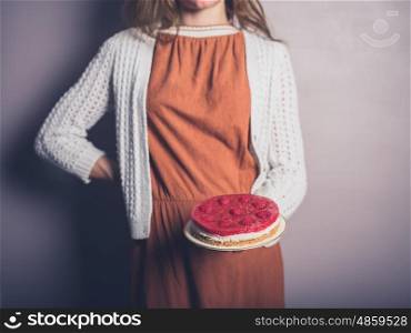 A young woman is proudly holding a rapberry cheesecakes she has made